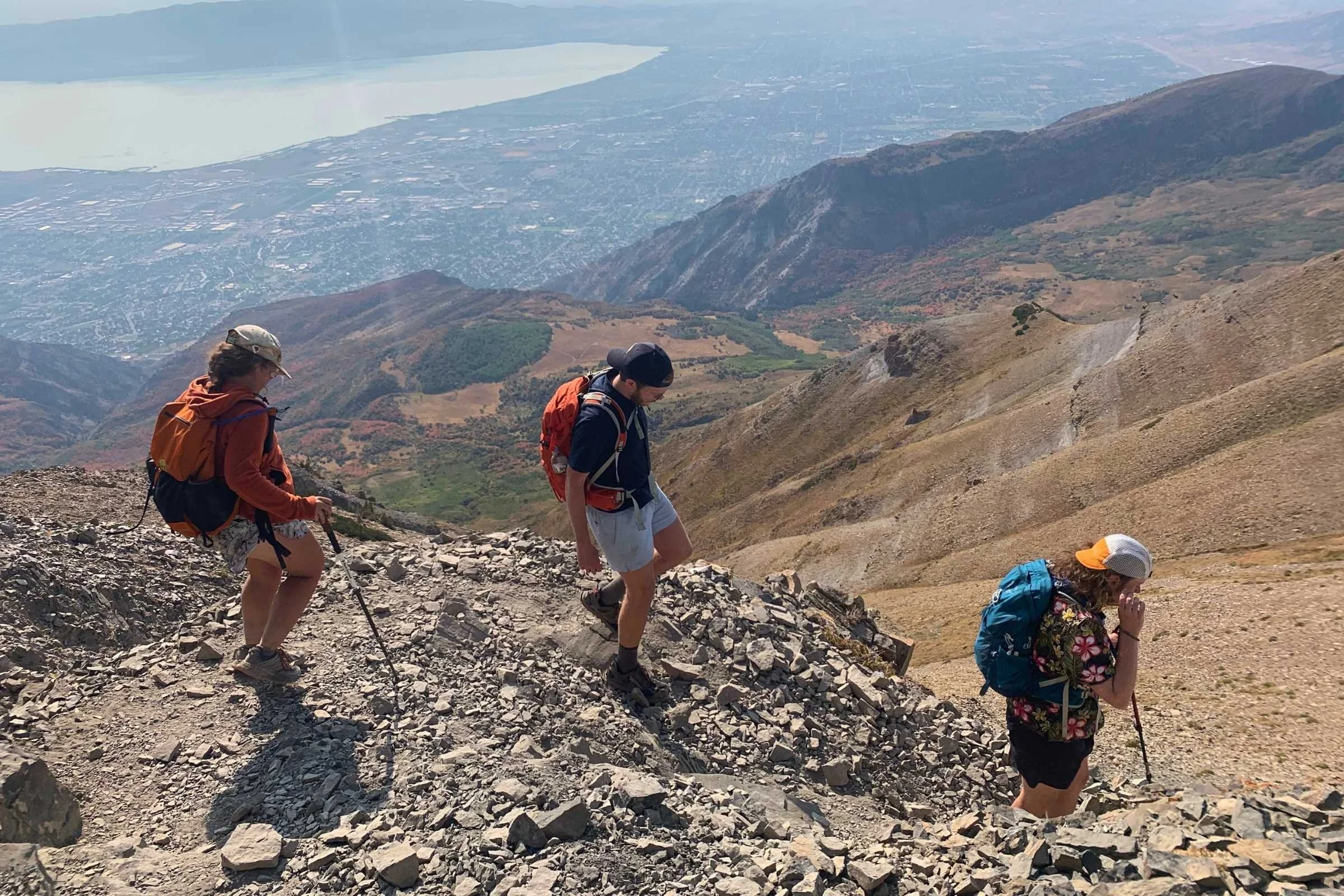 Two hikers adjusting and comparing different daypacks while standing on a mountain trail.